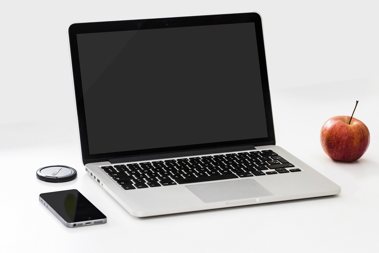 Zdjęcie przedstawia otwarty laptop, obok którego leży m.in. telefon komórkowy 