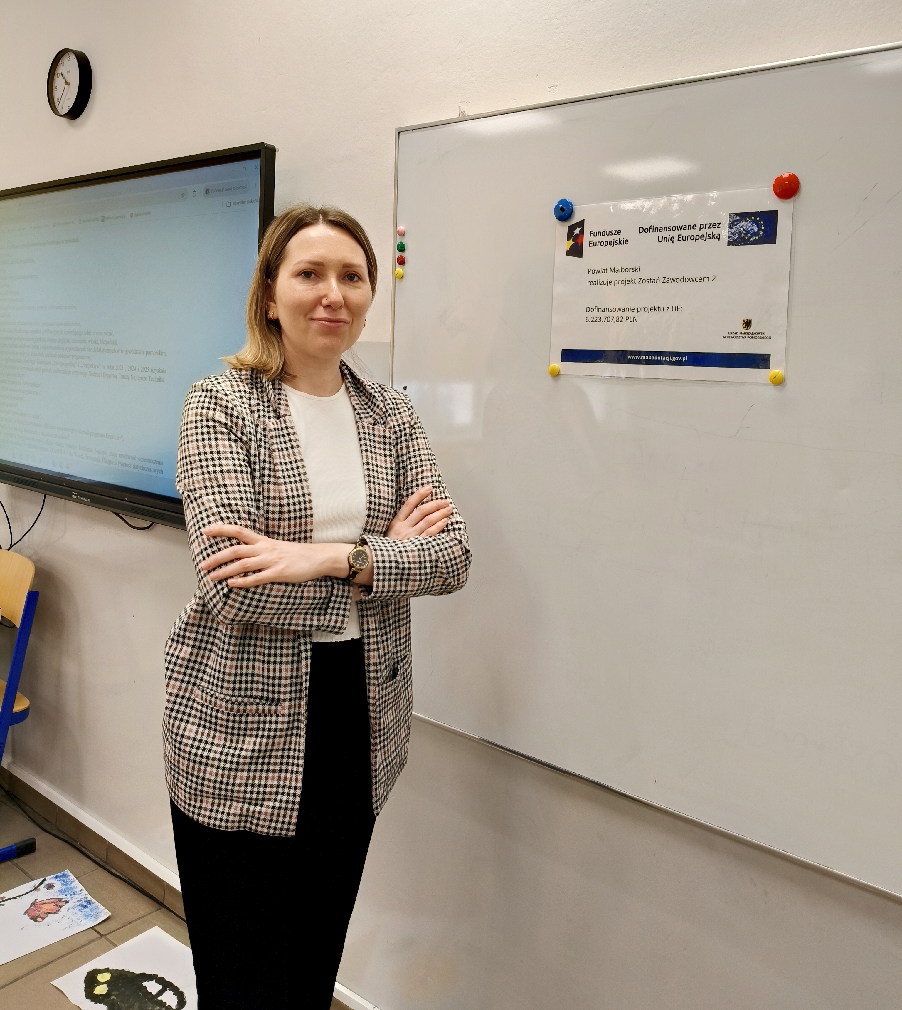 Zdjęcie przedstawia Koordynatorkę Powiatową stojącą przy tablicy, na której wisi plakat informujący o realizacji projektu "Zostań Zawodowcem 2"    